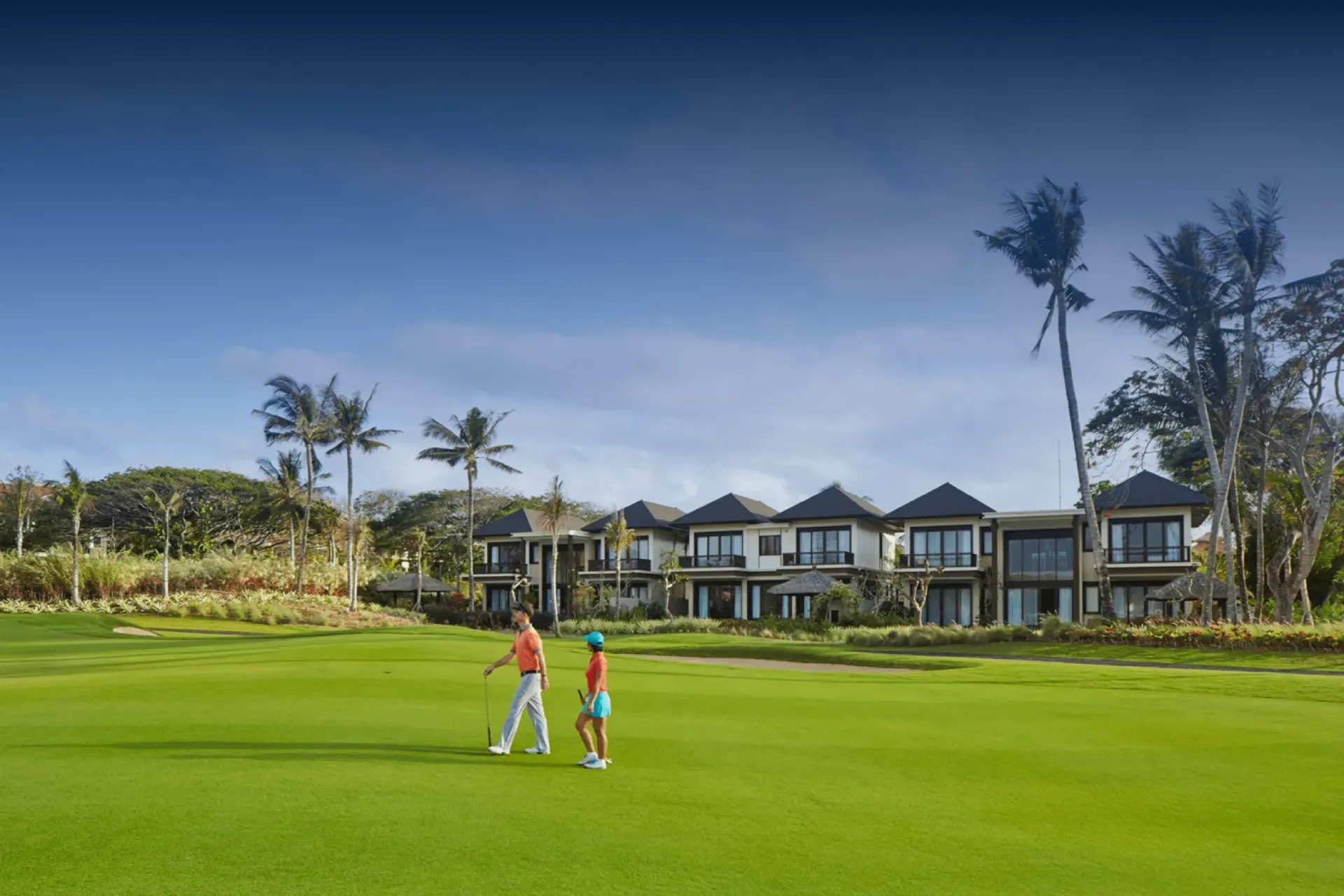 Two golfers walking a fairway past resort villas in Bali — golf and hotel arranged together by Bali Golf Tours